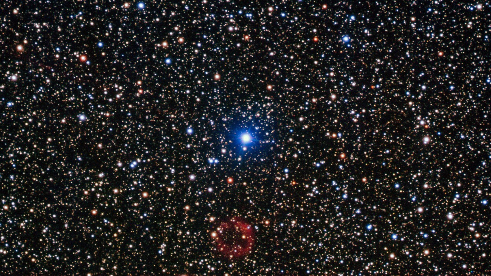 The bright star in the centre of this image is not the star of this show. At the bottom centre is a rather unremarkable smudge of red which is in fact a rare and valuable object. First discovered by amateur Japanese astronomer, Yukio Sakurai, in 1996, and noted as a nova-like object, Sakurai’s discovery turned out to be far more interesting than the supernova he initially supposed it to be. The object is actually a small white dwarf star undergoing a helium flash — one of only a handful of examples of such an event ever witnessed by astronomers. Normally, the white dwarf stage is the last in the life cycle of a low-mass star. In some cases, however, the star reignites in a helium flash and expands to return to a red giant state, ejecting huge amounts of gas and dust in the process, before once again shrinking to become a white dwarf. It is a dramatic and short-lived series of events, and Sakurai’s Object has allowed astronomers a very rare opportunity to study the events in real time. The white dwarf emits sufficient ultraviolet radiation to illuminate the gas it has expelled, which can just be seen in this image as the ring of red material. This image was taken using the FORS instrument, mounted on ESO’s Very Large Telescope.