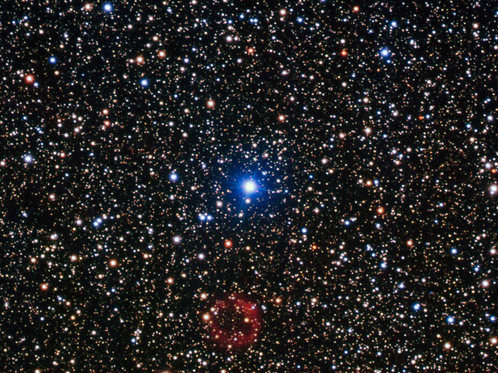 The bright star in the centre of this image is not the star of this show. At the bottom centre is a rather unremarkable smudge of red which is in fact a rare and valuable object. First discovered by amateur Japanese astronomer, Yukio Sakurai, in 1996, and noted as a nova-like object, Sakurai’s discovery turned out to be far more interesting than the supernova he initially supposed it to be. The object is actually a small white dwarf star undergoing a helium flash — one of only a handful of examples of such an event ever witnessed by astronomers. Normally, the white dwarf stage is the last in the life cycle of a low-mass star. In some cases, however, the star reignites in a helium flash and expands to return to a red giant state, ejecting huge amounts of gas and dust in the process, before once again shrinking to become a white dwarf. It is a dramatic and short-lived series of events, and Sakurai’s Object has allowed astronomers a very rare opportunity to study the events in real time. The white dwarf emits sufficient ultraviolet radiation to illuminate the gas it has expelled, which can just be seen in this image as the ring of red material. This image was taken using the FORS instrument, mounted on ESO’s Very Large Telescope.